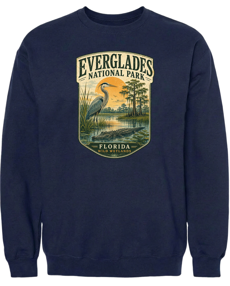 A navy blue sweatshirt with a graphic design depicting a bird, likely a heron, standing in a marshy area with trees and a sunset in the background.