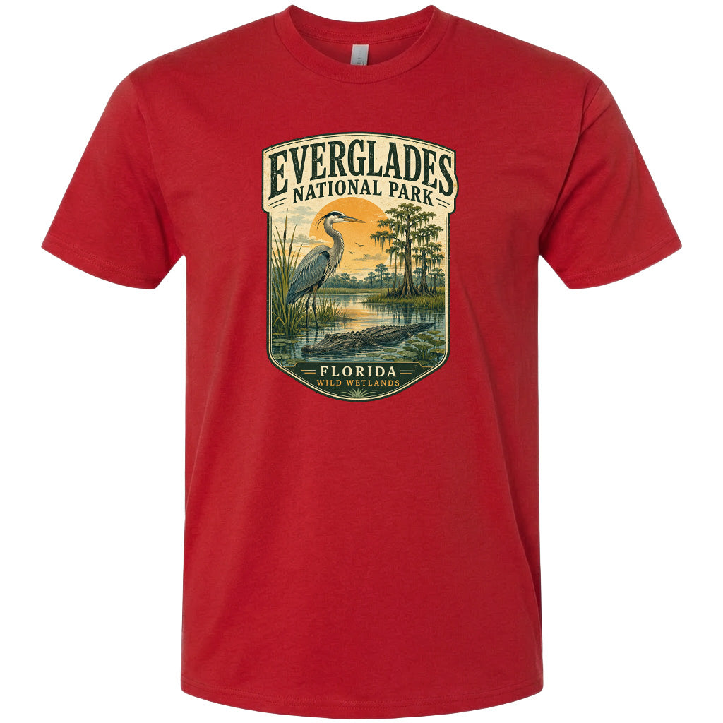 A red t-shirt with a graphic design depicting a bird, a pond, and trees, along with the text "EVERGLADES NATIONAL PARK FLORIDA WILD WETLANDS".