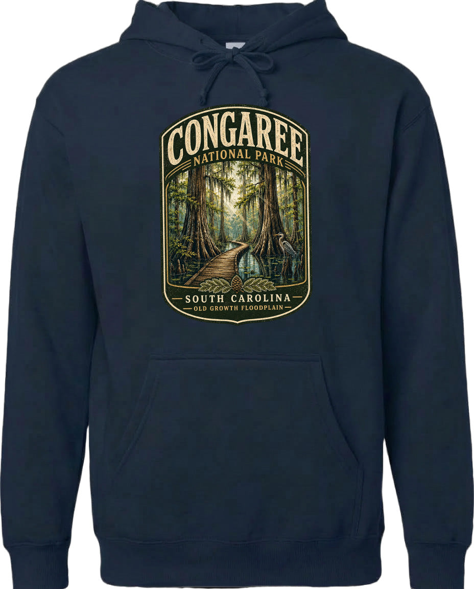 A navy blue hoodie with a graphic design depicting a forest scene, featuring a path leading through the trees and the text "CONGAREE NATIONAL PARK SOUTH CAROLINA OLD GROWTH FLOODPLAIN".