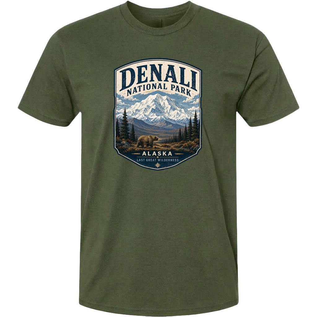 A green t-shirt with a graphic design depicting a mountain landscape with a bear in the foreground, surrounded by pine trees and mountains.