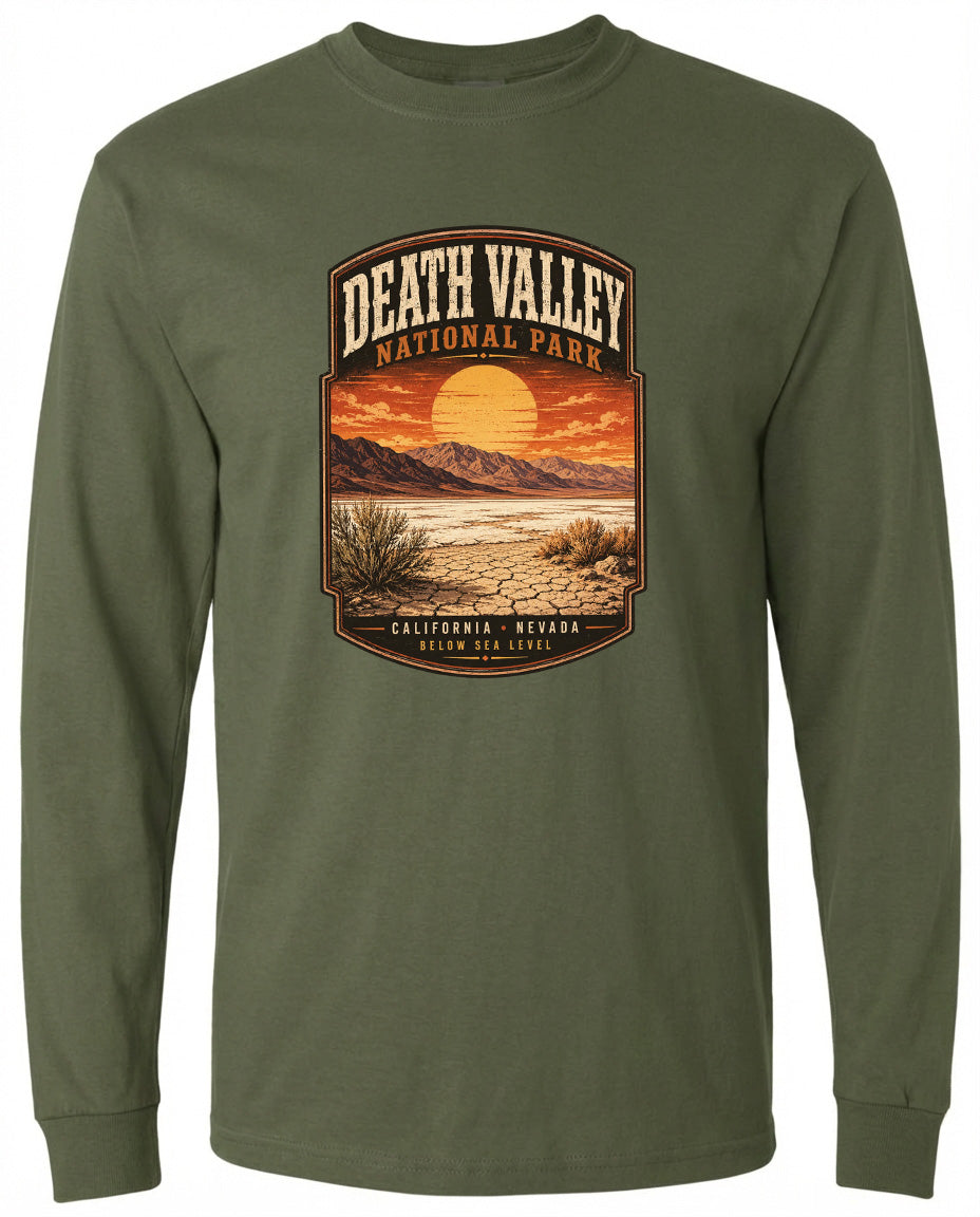 A long-sleeved green t-shirt with a graphic design depicting a desert landscape with mountains, a sunset, and a label that reads "DEATH VALLEY NATIONAL PARK CALIFORNIA NEVADA BELOW SEA LEVEL".