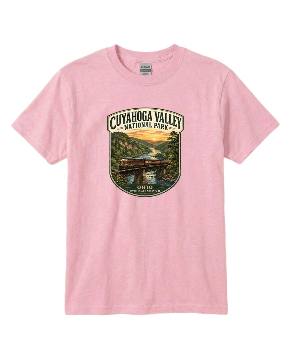 A pink t-shirt with a graphic design depicting a scenic view of the Cuyaohoga Valley National Park, featuring a bridge, river, and sunset.