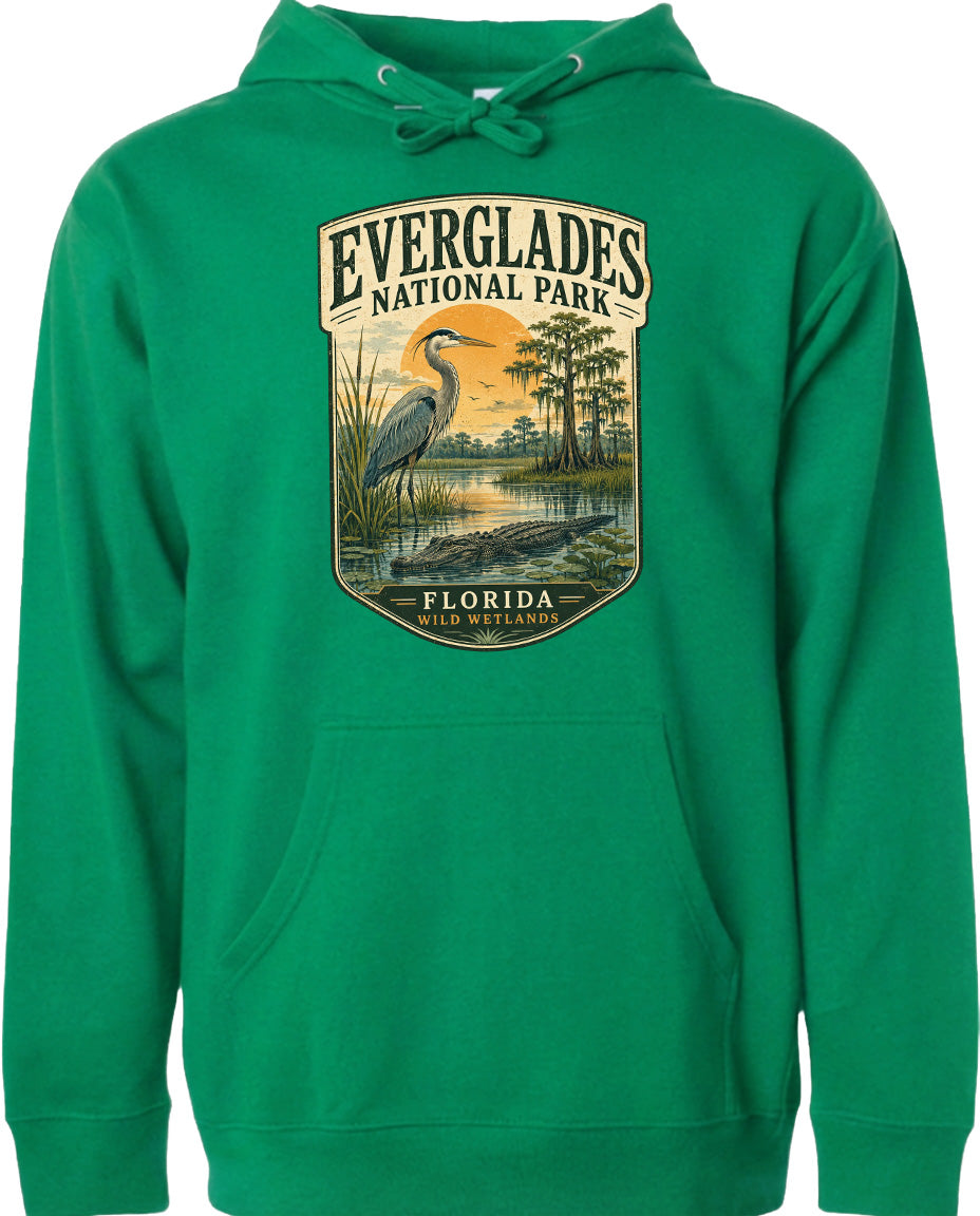 A green hoodie with a graphic design depicting a bird standing in a marshy area with trees and a sunset in the background.