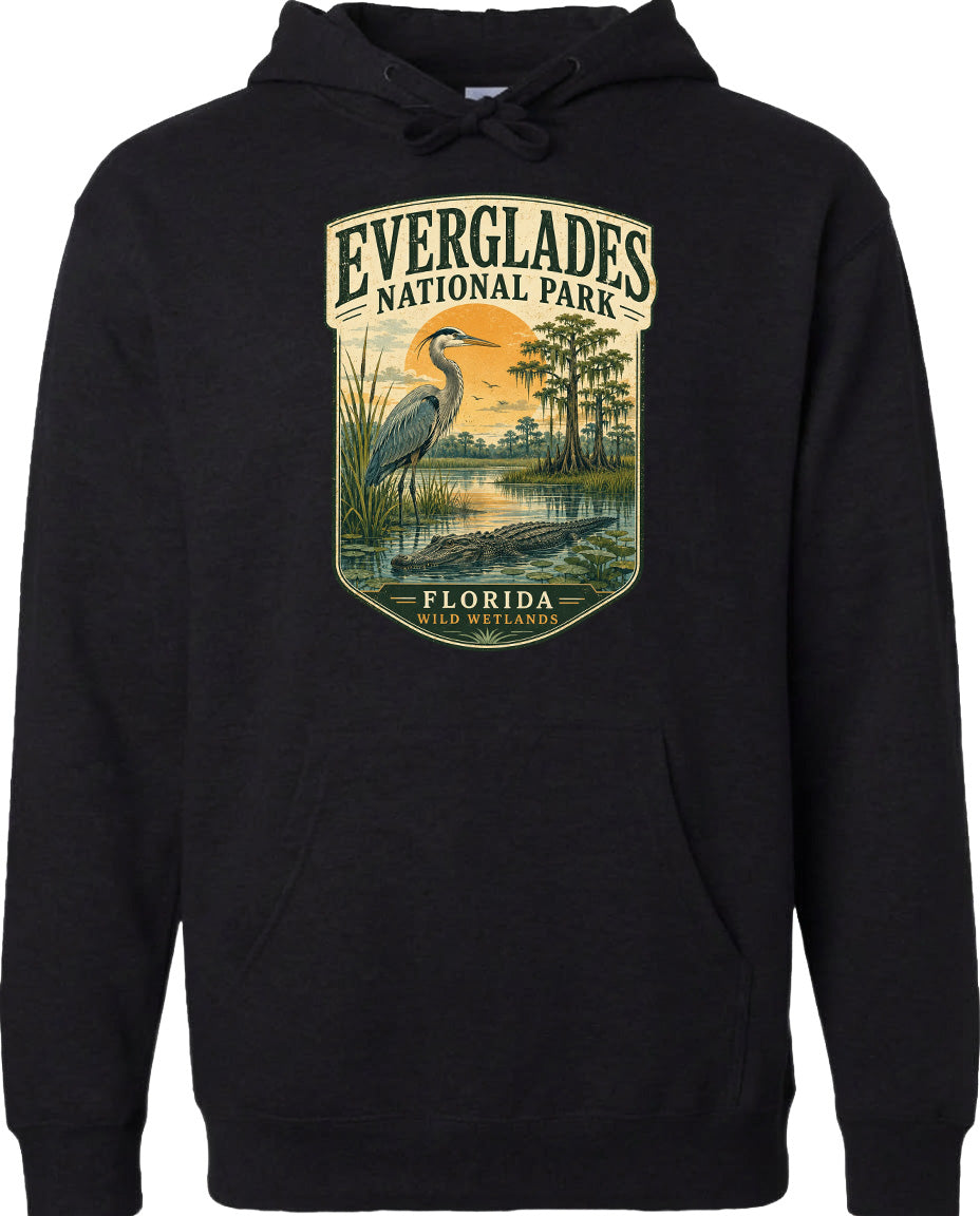 A black hoodie with a graphic design depicting a heron standing in a marshy area with trees and a sunset in the background.