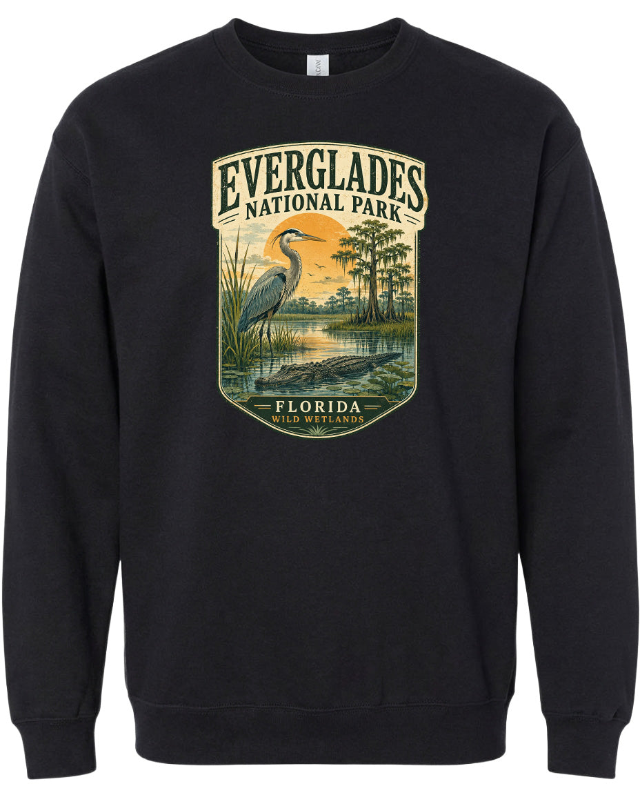 A black sweatshirt with a graphic design depicting a bird, likely a heron, standing in a marshy area with trees and a sunset in the background.