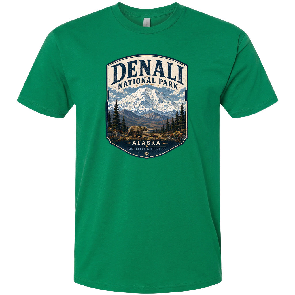 A green t-shirt with a graphic design depicting a mountain landscape with a bear in the foreground, surrounded by pine trees and mountains.