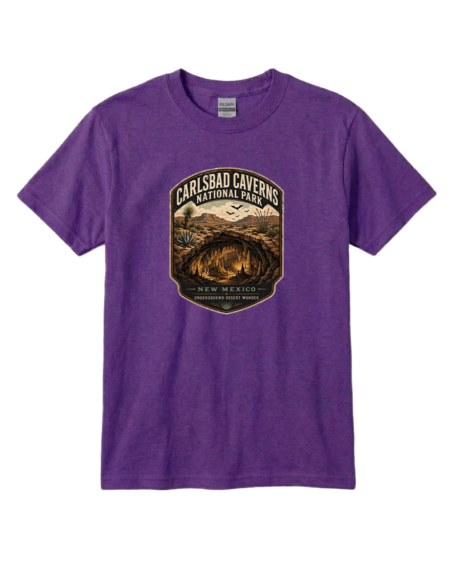 A purple t-shirt with a graphic design featuring a shield-shaped emblem that says "CARLSBAD CAVENS NATIONAL PARK NEW MEXICO UNDERGROUND WONDERS".