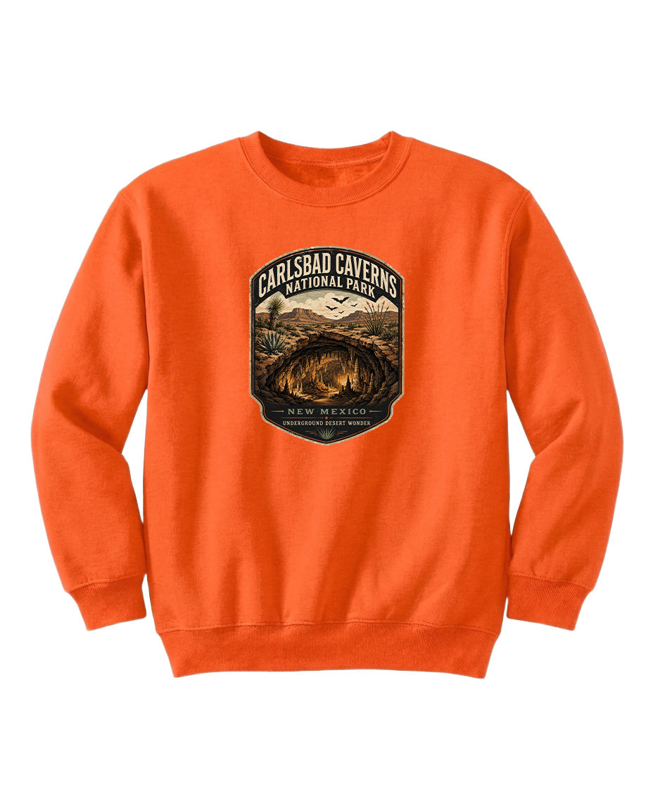 An orange sweatshirt with a graphic design featuring a cave and mountains, along with the text "CARLSBAD CAVENS NATIONAL PARK" and "NEW MEXICO UNDERGROUND WONDER".