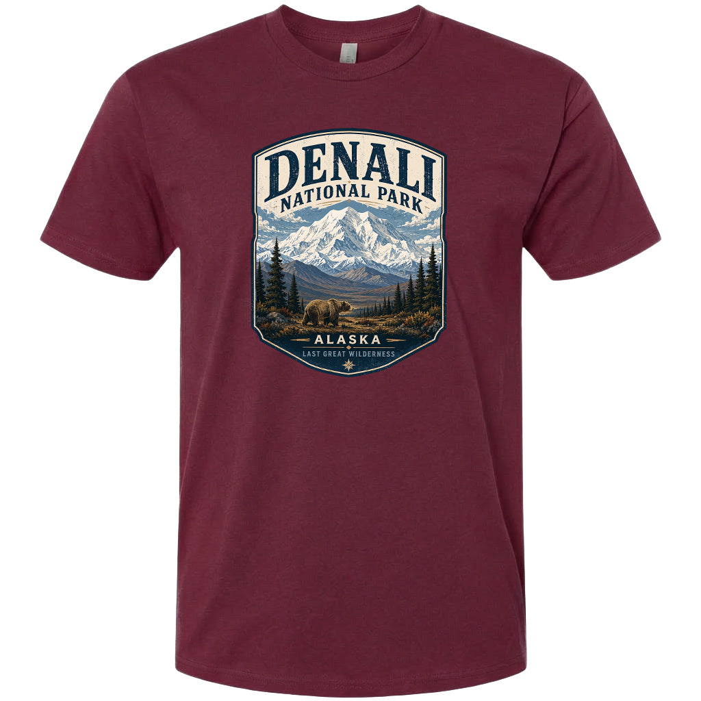 A maroon t-shirt with a graphic design depicting a mountain landscape with a bear in the foreground, surrounded by pine trees and mountains.