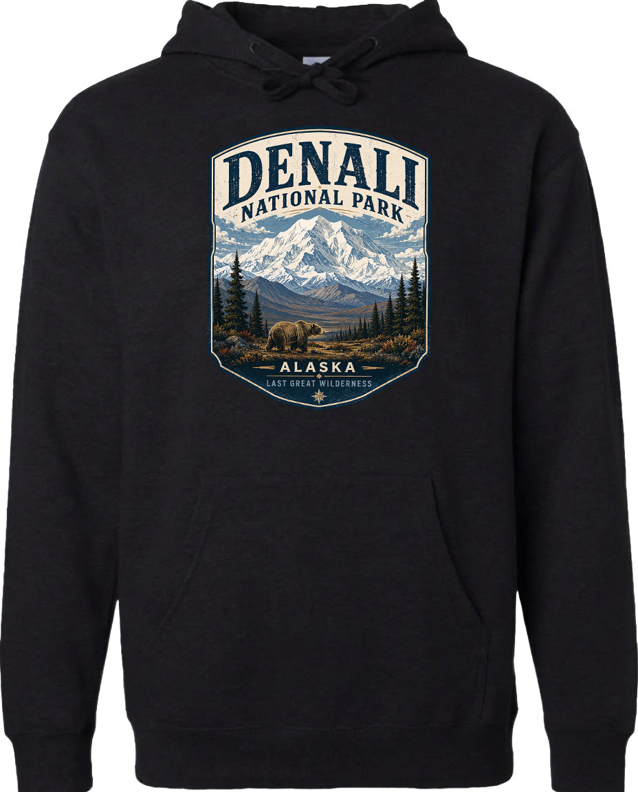 A black hoodie with a graphic design depicting a scenic landscape of Denali National Park in Alaska, featuring a mountain range, pine trees, and a bear.