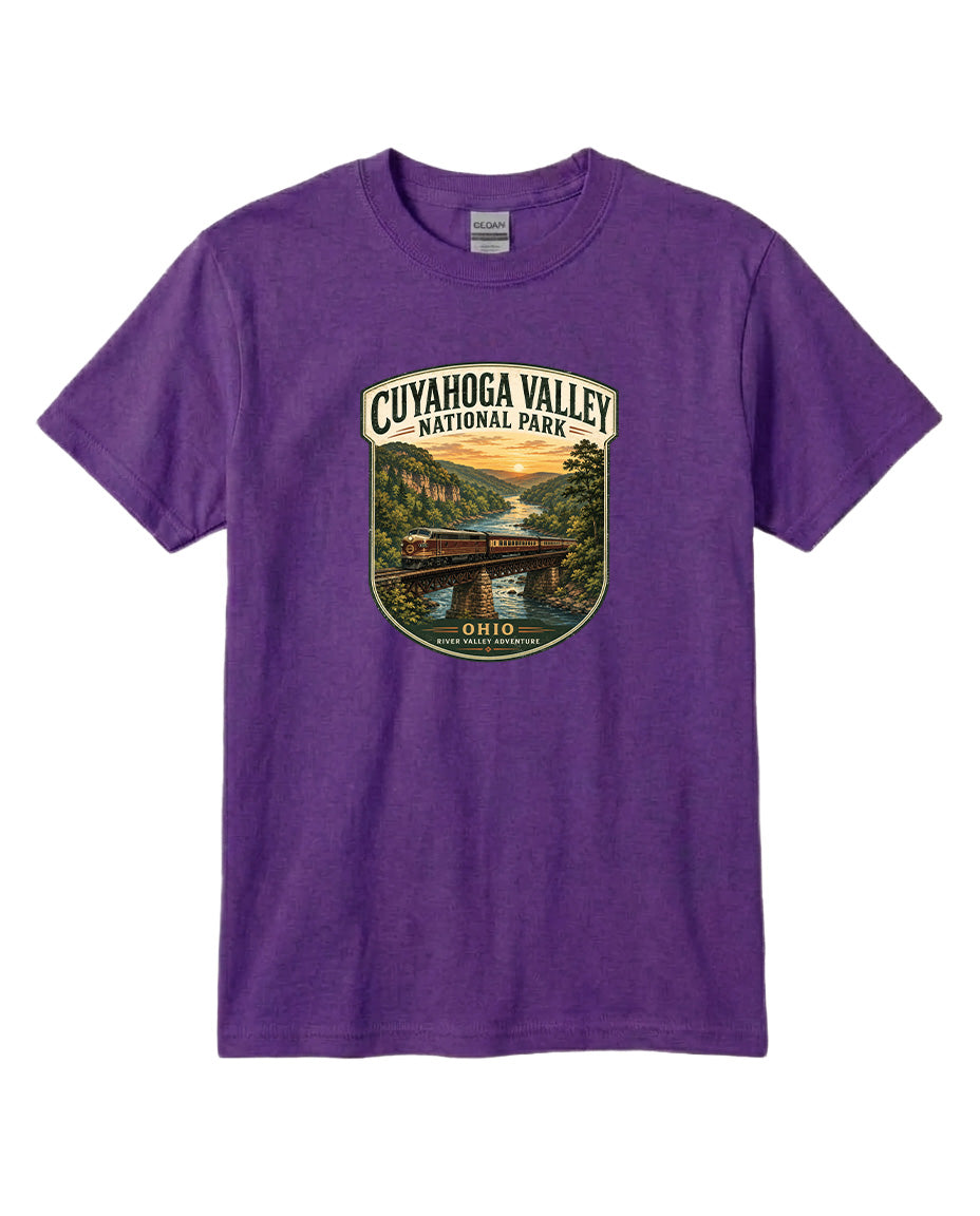 A purple t-shirt with a graphic design depicting a scenic view of the Cuyaños Valley National Park, featuring a bridge, river, and sunset.