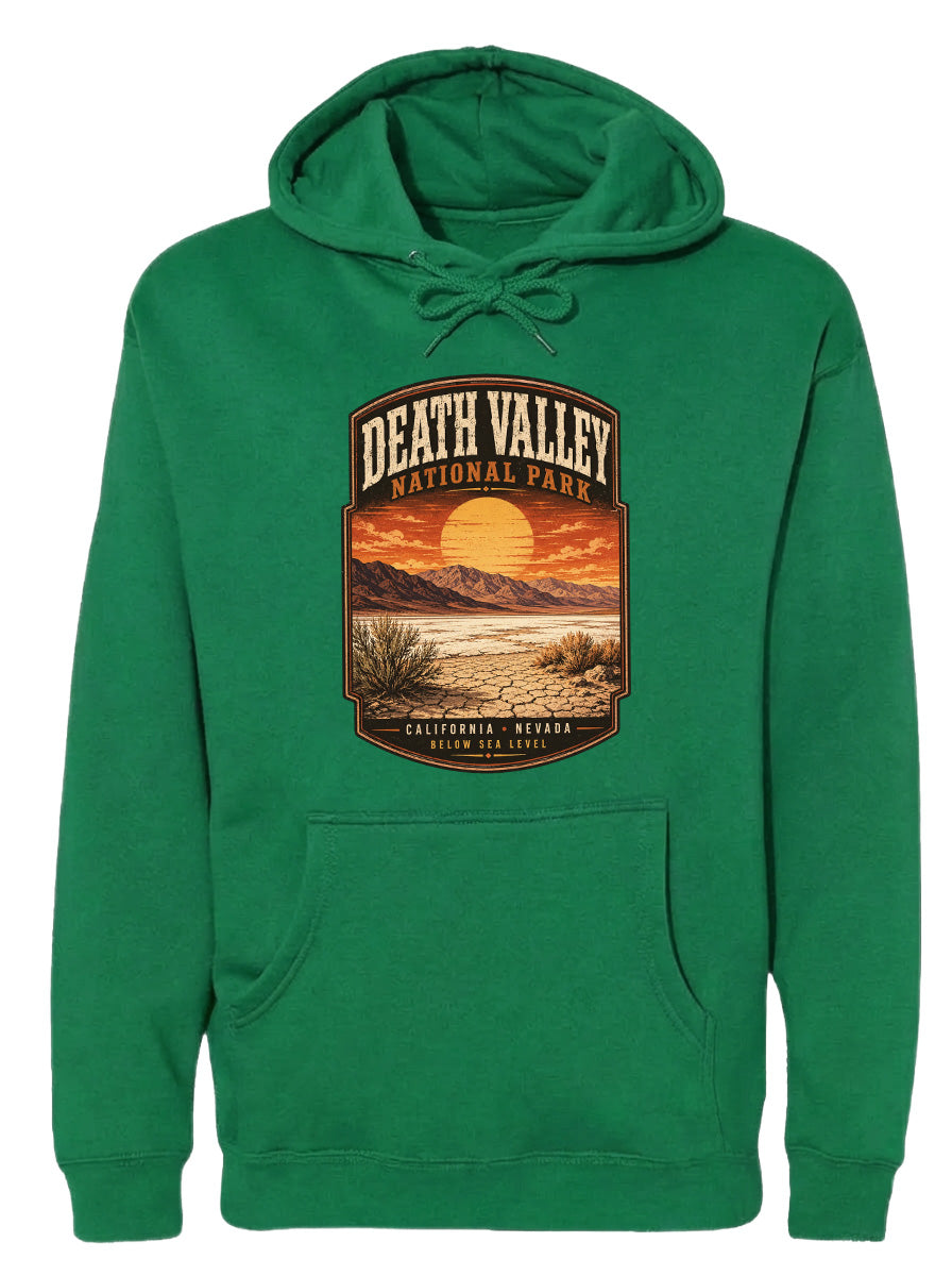 A green hoodie with a graphic design depicting Death Valley National Park, including a sunset over the mountains and desert landscape.