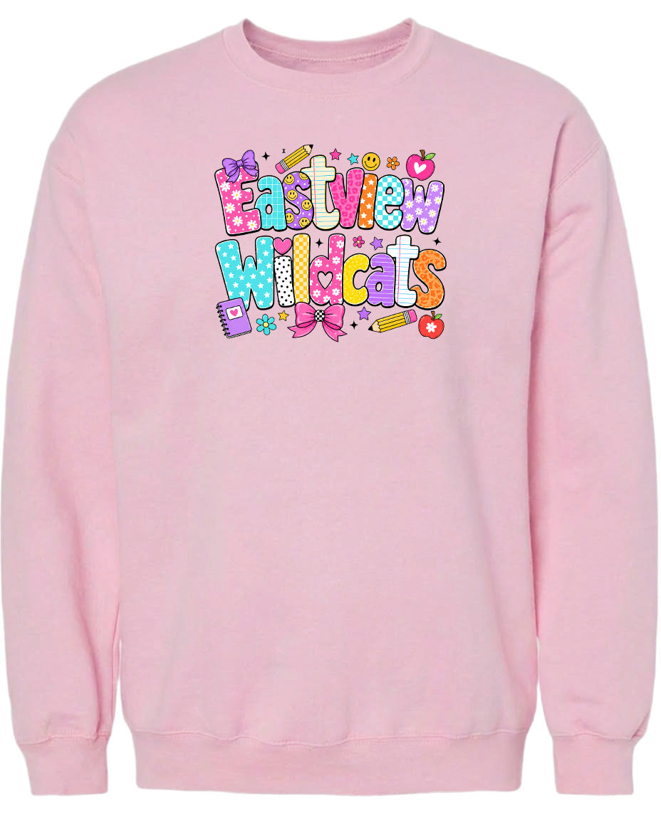 A pink sweatshirt with a colorful graphic design featuring the text "Eastview Wildcats" and various decorative elements such as stars, hearts, and a pencil.