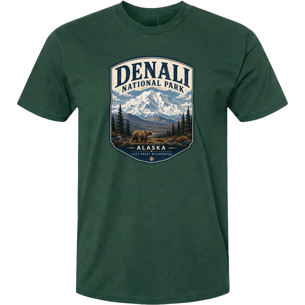 A green t-shirt with a graphic design depicting a mountain landscape with a bear in the foreground, surrounded by pine trees and mountains.