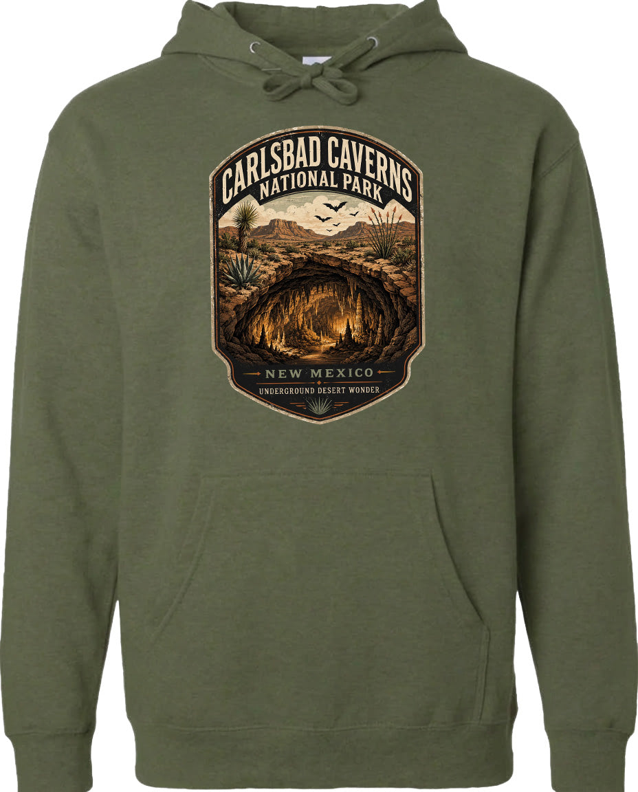 A hoodie with a graphic design featuring a desert landscape with a cave or tunnel, surrounded by mountains and cacti. The text above the design reads "CARLSBAD CAVENS NATIONAL PARK" and below it says "NEW MEXICO UNDERGROUND INTELLIGENT WONDER".