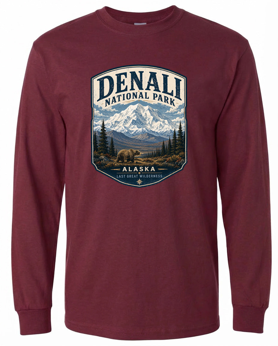 A long-sleeved burgundy t-shirt with a graphic design featuring a mountain landscape with a bear in the foreground, surrounded by pine trees.