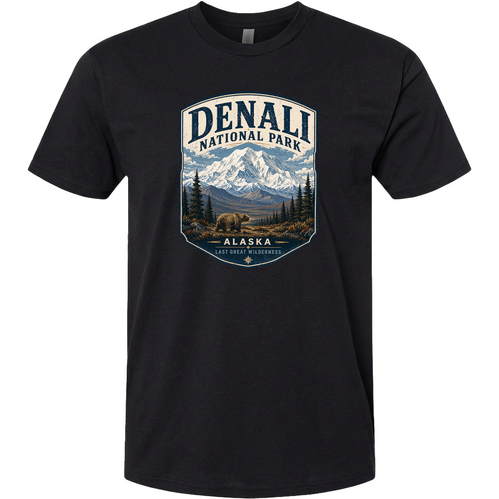 A black t-shirt with a graphic design depicting a mountain landscape with a bear in the foreground, surrounded by pine trees and mountains.