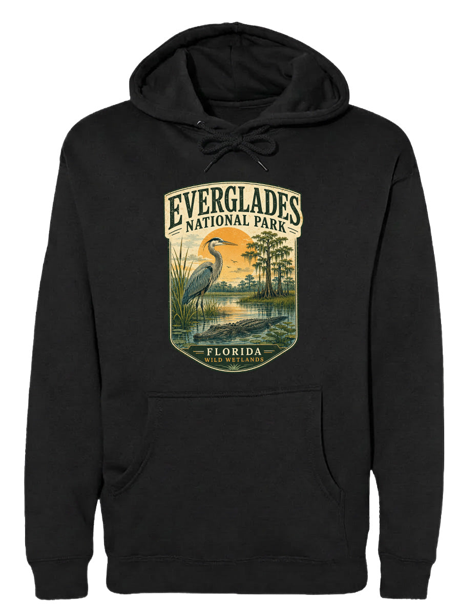 A black hoodie with a graphic design depicting a bird, likely a heron, standing in a marshy area with trees and a sunset in the background.