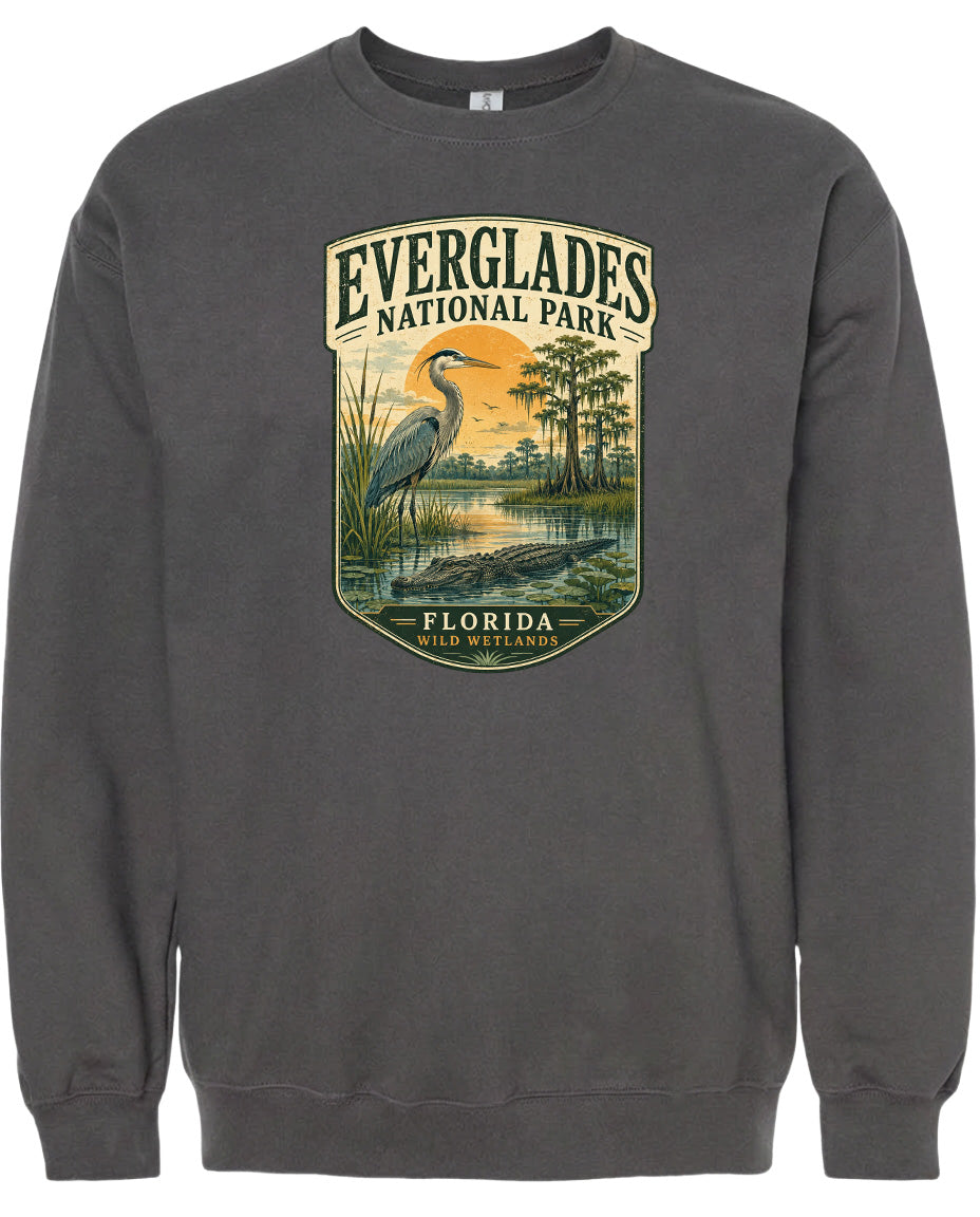 A gray sweatshirt with a graphic design depicting a bird, likely a heron, standing in a marshy area with trees and a sunset in the background.