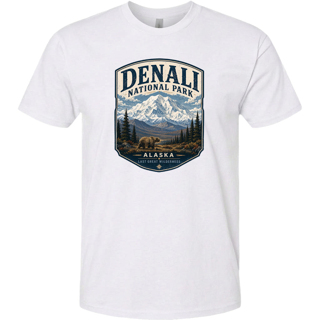 A white t-shirt with a graphic design depicting a mountain landscape with a bear in the foreground, surrounded by pine trees and mountains.