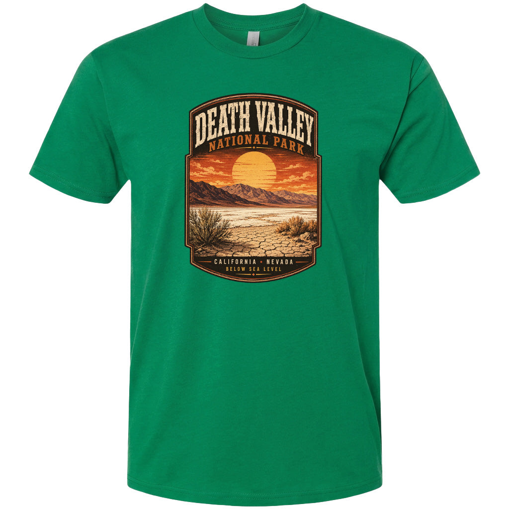 A green t-shirt with a graphic design depicting a desert landscape with mountains, a sunset, and a label that reads "DEATH VALLEY NATIONAL PARK CALIFORNIA NEVADA BELOW SEA LEVEL".