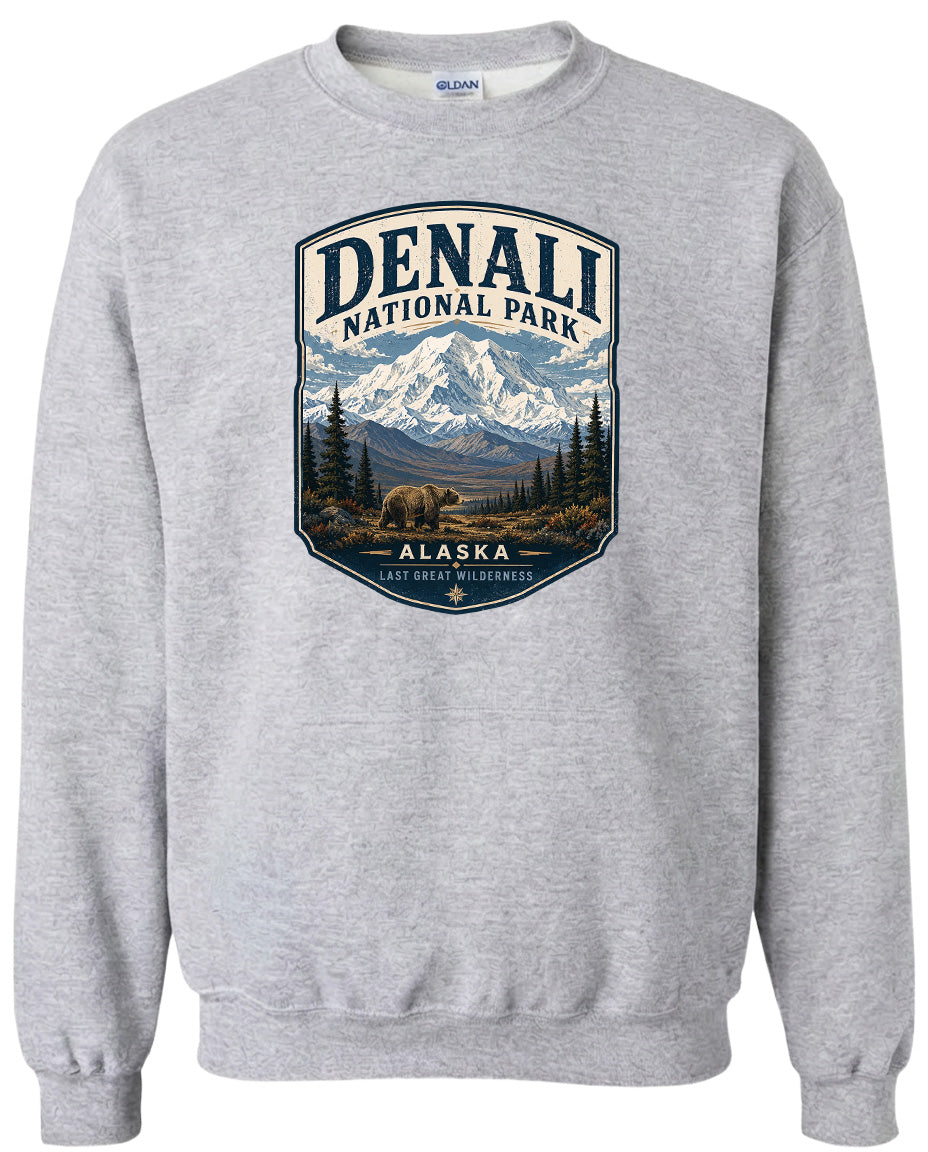 A gray sweatshirt with a graphic design depicting a mountain landscape with a bear in the foreground, surrounded by pine trees and mountains.