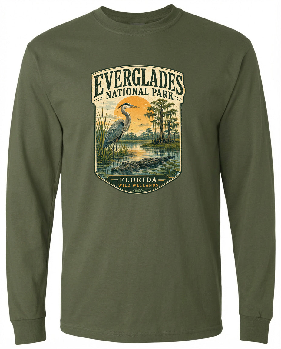A long-sleeved green t-shirt with a graphic design depicting a bird, a pond, and trees, along with the text "EVERGLADES NATIONAL PARK FLORIDA WILD WETLANDS".