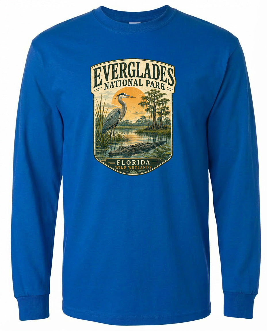 A blue long-sleeved t-shirt with a graphic design depicting a bird standing in a pond surrounded by trees and a sunset.