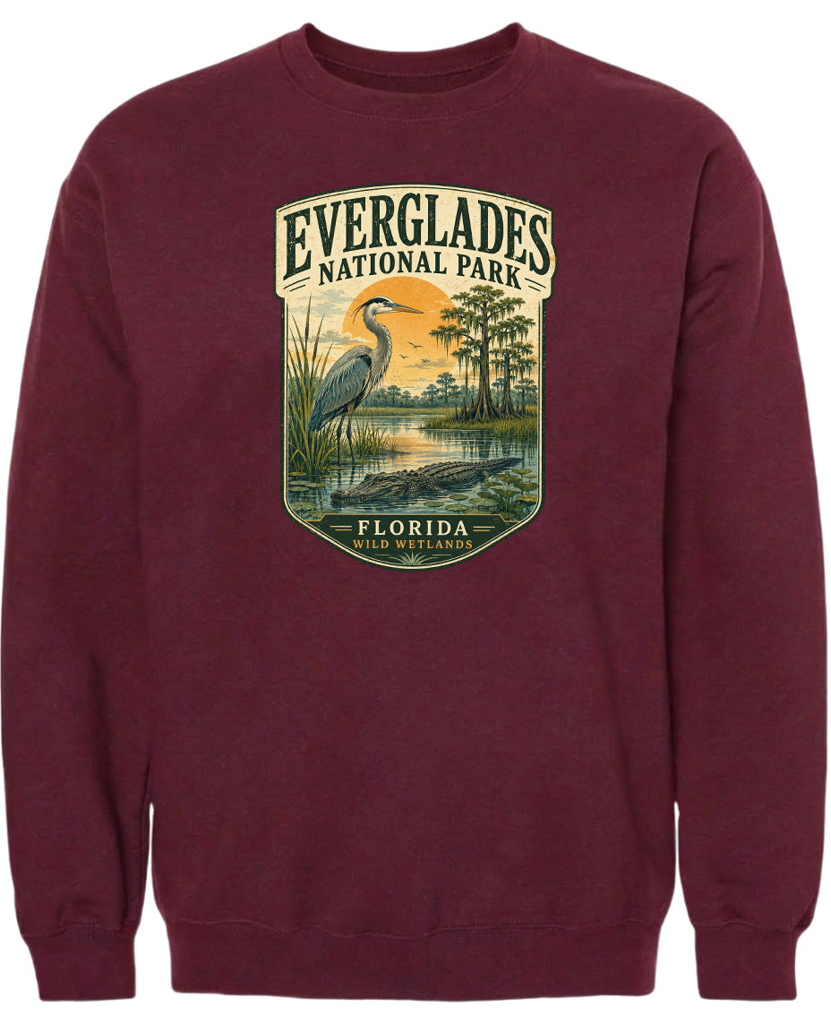 A maroon sweatshirt with a graphic design depicting a bird, likely a heron, standing in a marshy area with trees and a sunset in the background.