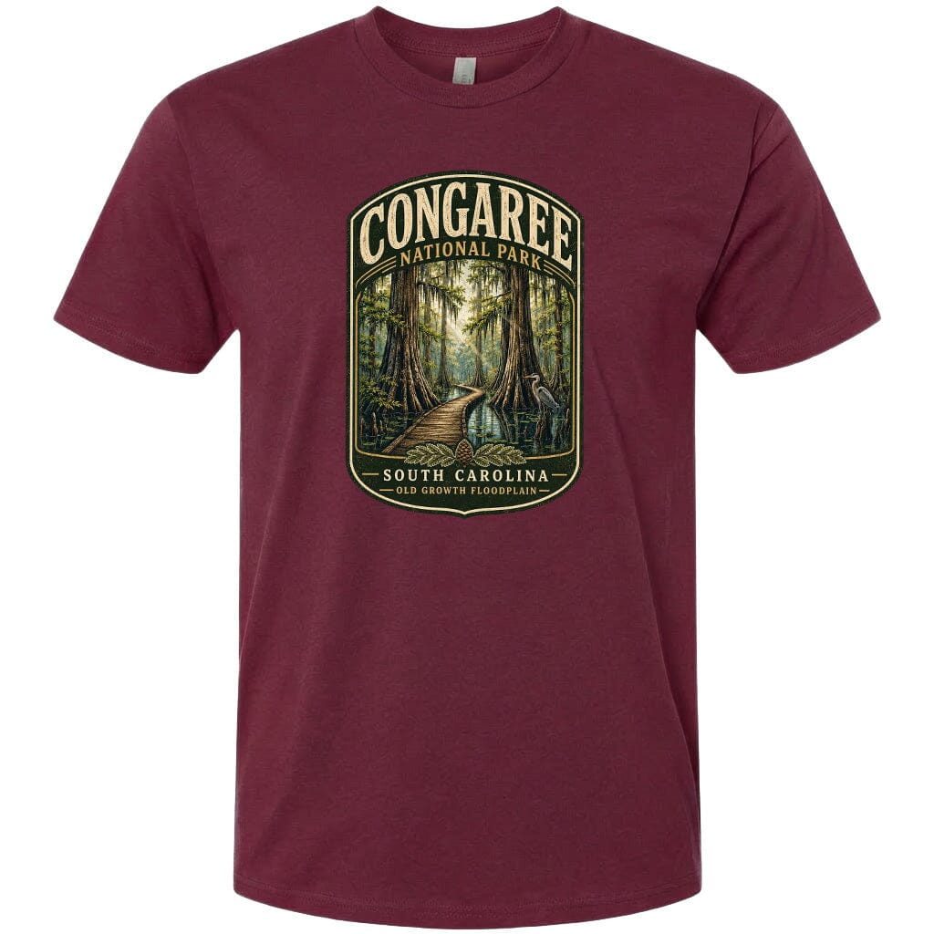 A maroon t-shirt with a graphic design depicting a forest scene, including a path leading through the trees and a body of water in the background.