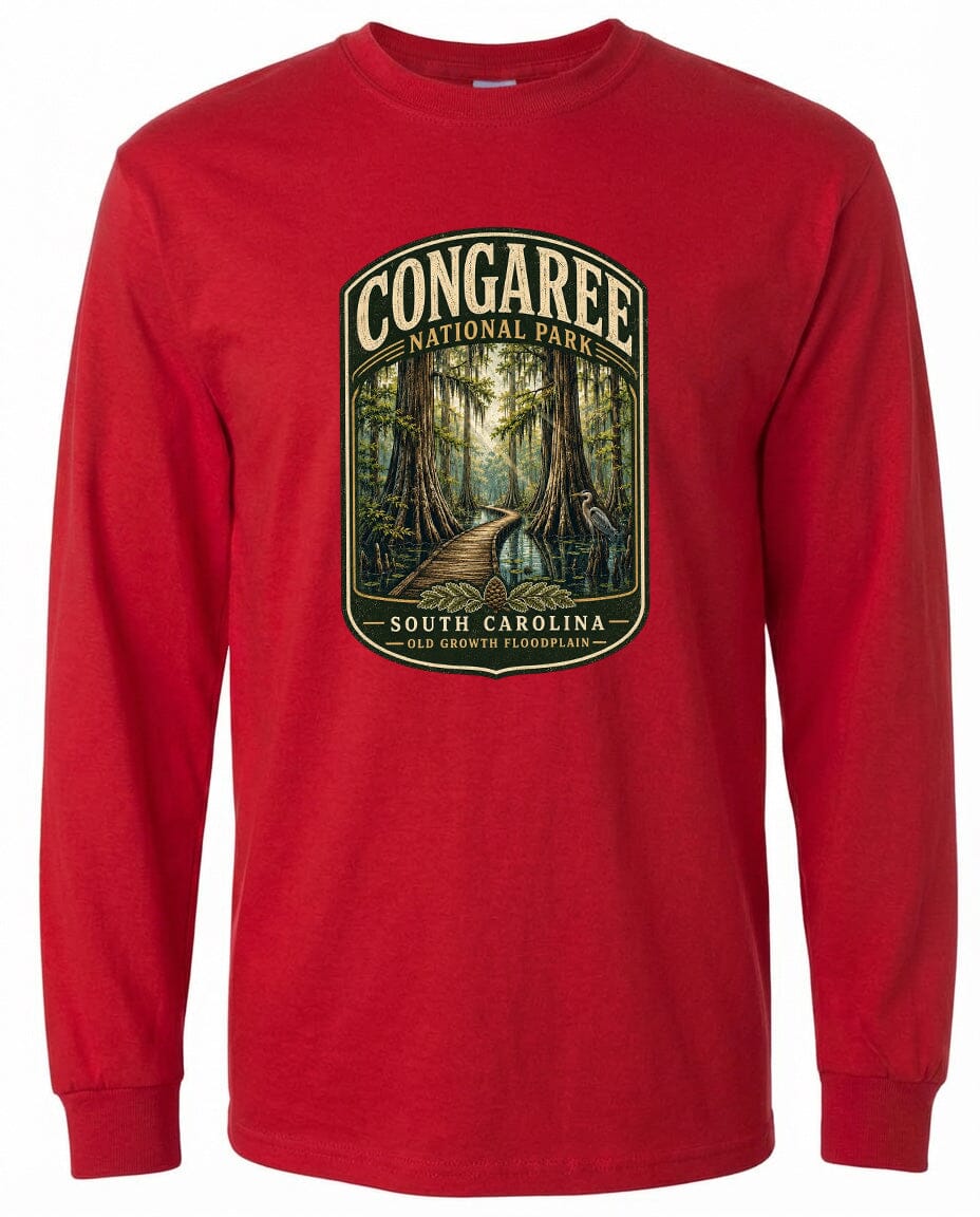 A red long-sleeved t-shirt with a graphic design depicting a forest scene, featuring a path leading through the trees and the text "CONGAREE NATIONAL PARK SOUTH CAROLINA OLD GROWTH FLOODPLAIN".
