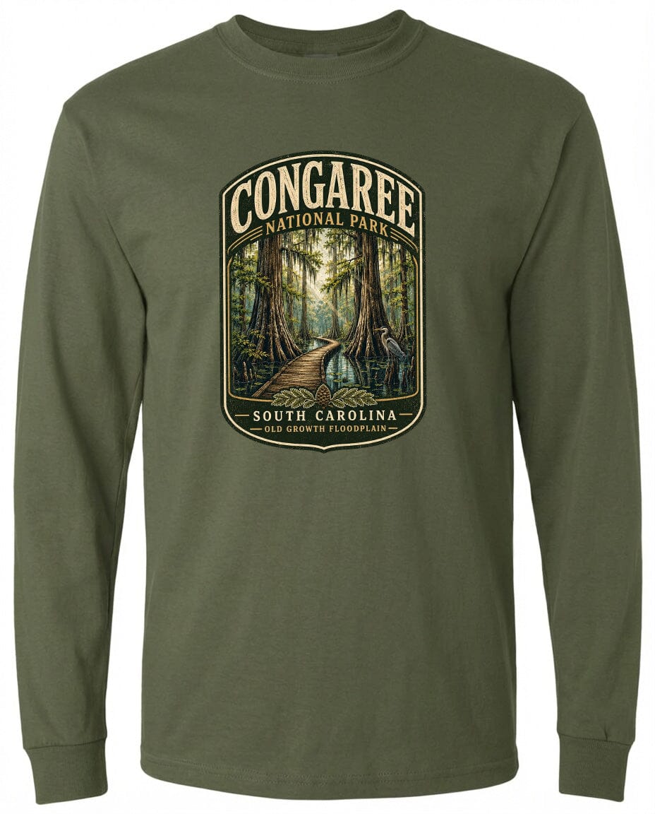 A green long-sleeved t-shirt with a graphic design depicting a forest scene, featuring a path leading through the trees and the text "CONGAREE NATIONAL PARK SOUTH CAROLINA OLD GROWTH FLOODPLAIN".