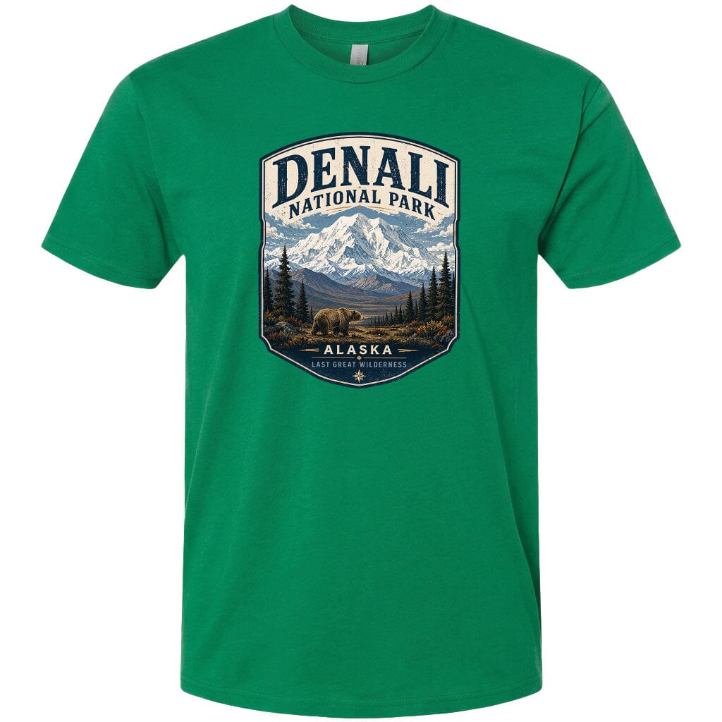 A green t-shirt with a graphic design depicting a mountain landscape with a bear in the foreground, surrounded by pine trees and mountains.