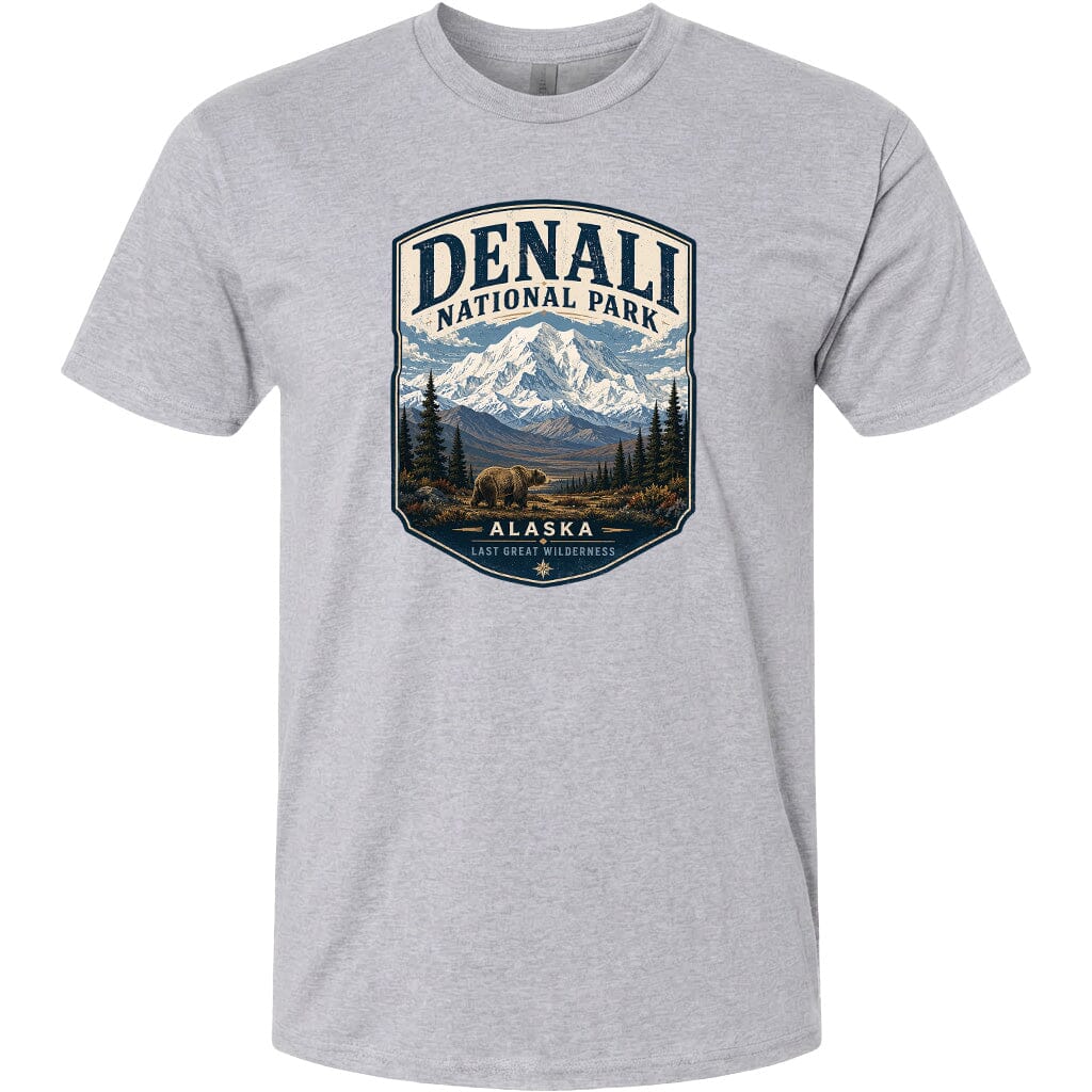 A gray t-shirt with a graphic design depicting a mountain landscape with a bear in the foreground, surrounded by pine trees and mountains.