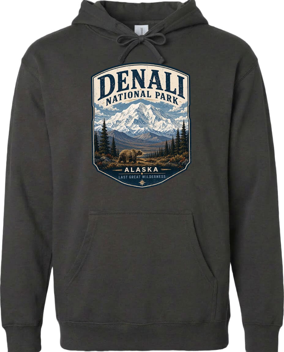 A hoodie with a graphic design featuring a mountain landscape with a bear in the foreground, surrounded by pine trees and mountains.