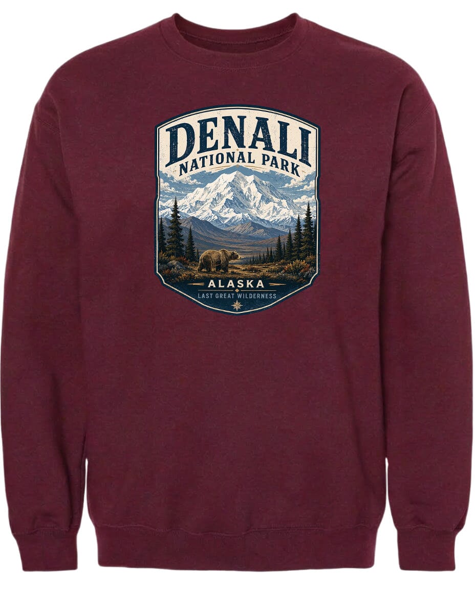 A burgundy-colored sweatshirt with a graphic design depicting a mountain landscape with a bear in the foreground, surrounded by pine trees and mountains.