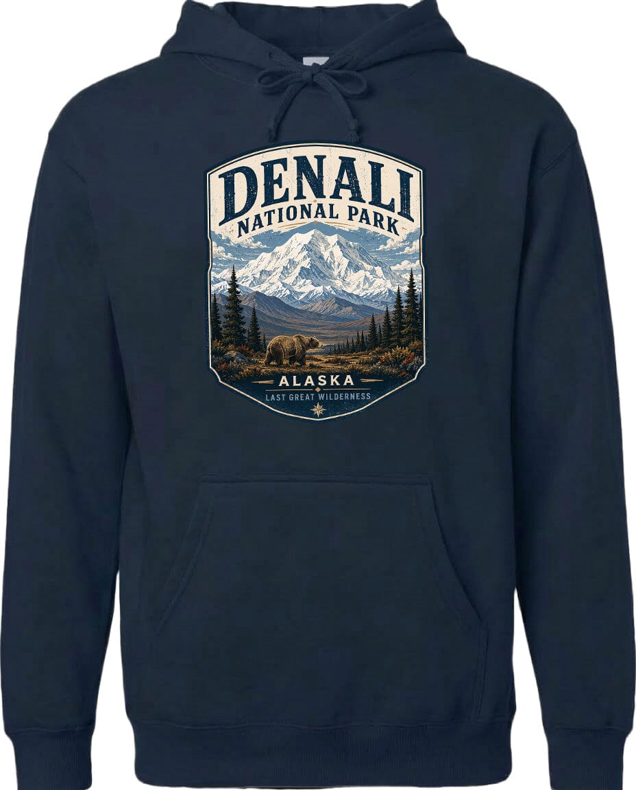 A hoodie with a graphic design featuring a mountain landscape with a bear in the foreground, surrounded by pine trees and mountains.