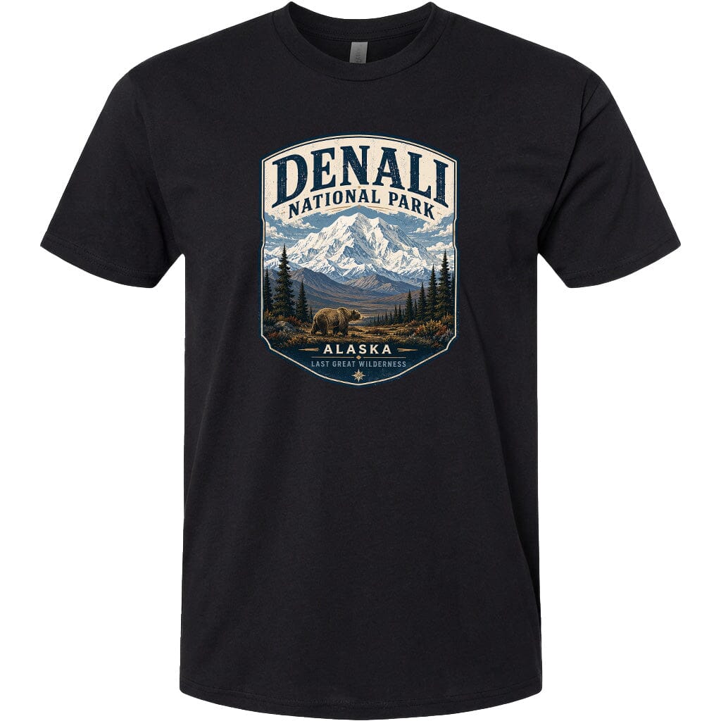 A black t-shirt with a graphic design depicting a mountain landscape with a bear in the foreground, surrounded by pine trees and mountains.