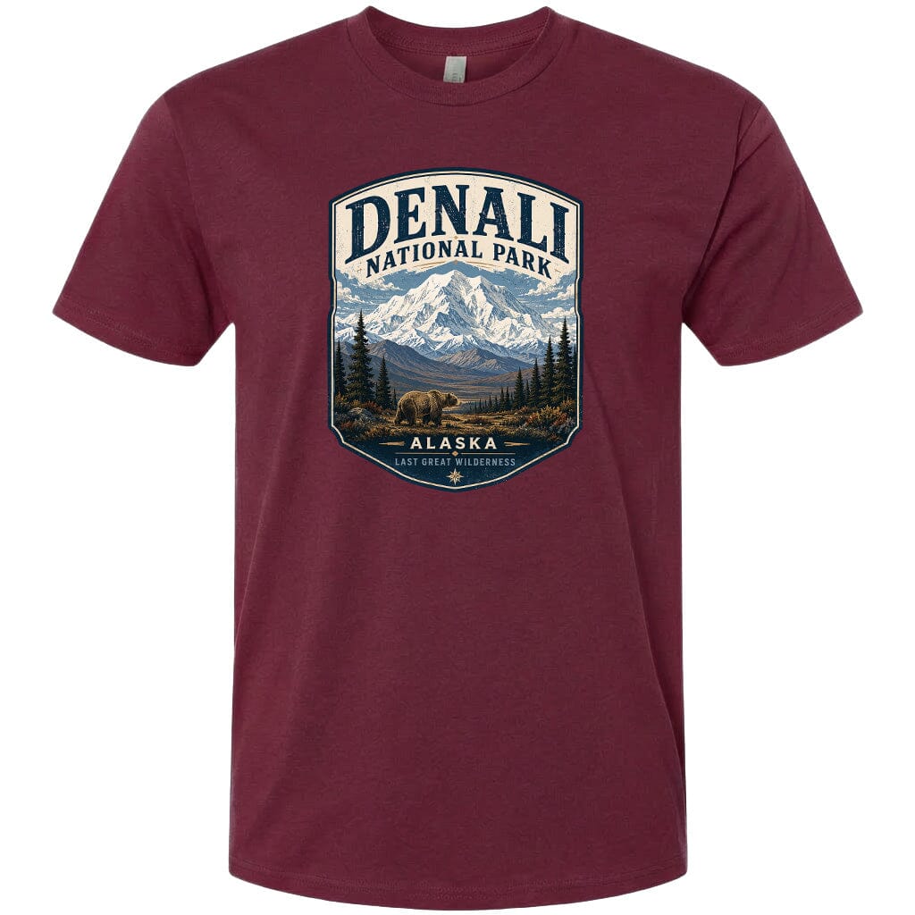 A maroon t-shirt with a graphic design depicting a mountain landscape with a bear in the foreground, surrounded by pine trees and mountains.