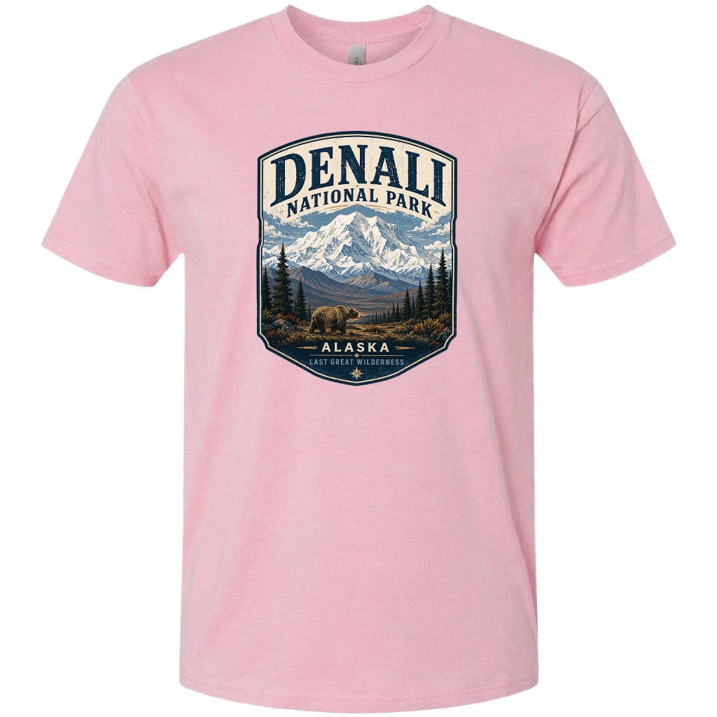 A pink t-shirt with a graphic design depicting a mountain landscape with a bear in the foreground, surrounded by pine trees and mountains.