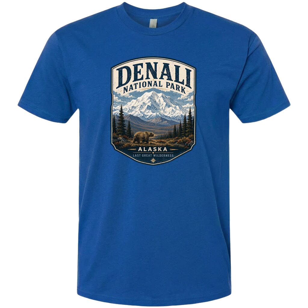 A blue t-shirt with a graphic design depicting a mountain landscape with a bear in the foreground, surrounded by pine trees and mountains.