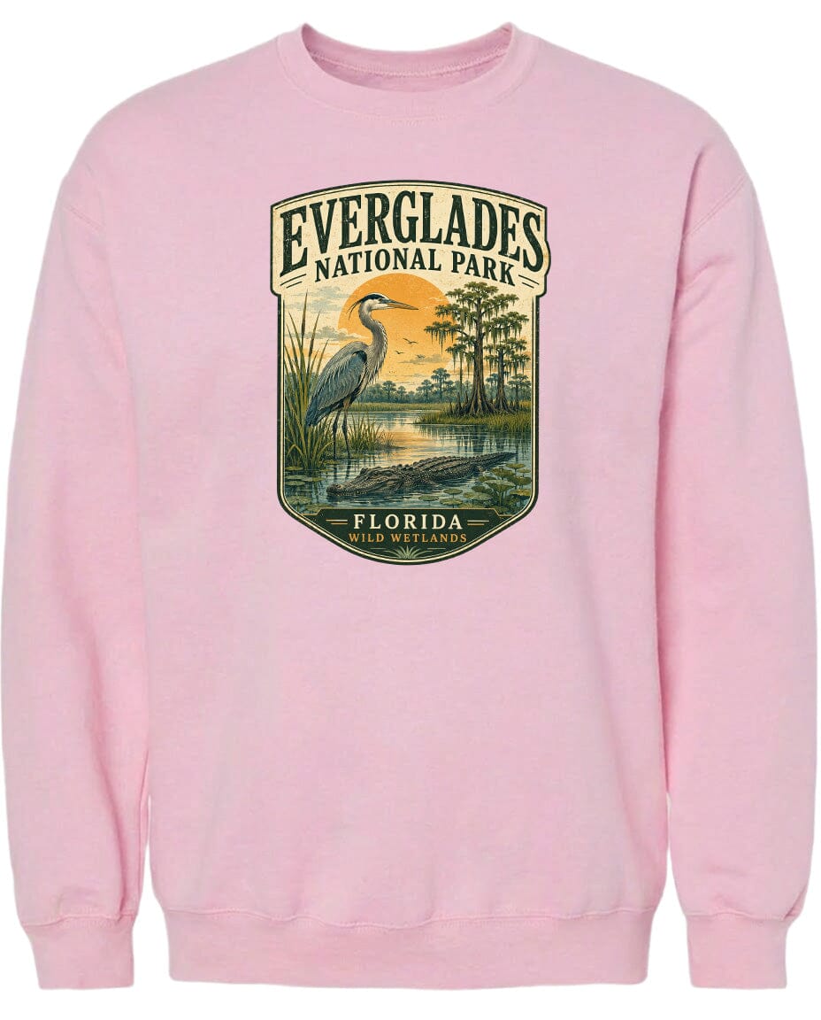 A pink sweatshirt with a graphic design depicting a bird, likely a heron, standing in a marshy area with trees and water.