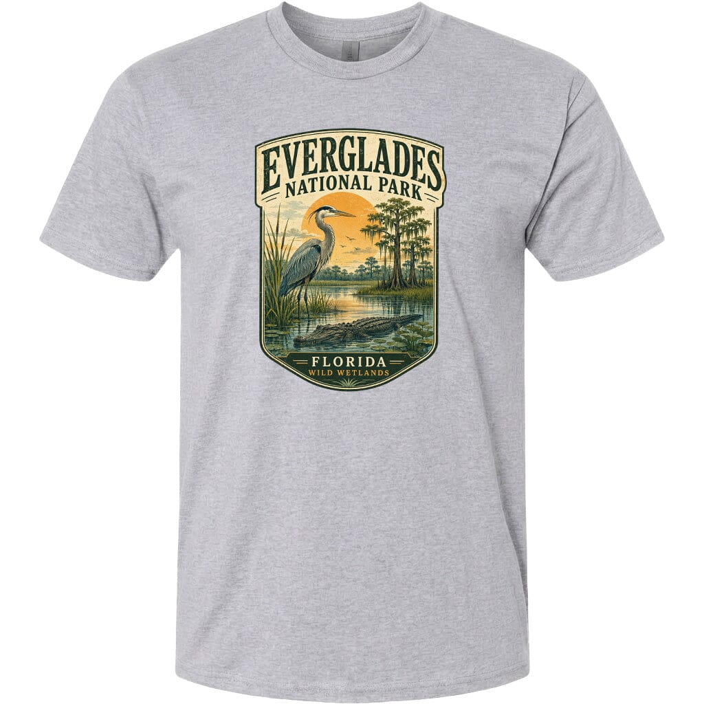 A gray t-shirt with a graphic design depicting a bird, a pond, and a landscape with trees and a sunset. The text on the t-shirt reads "EVERGLADES NATIONAL PARK FLORIDA WILD WESTLANDS".
