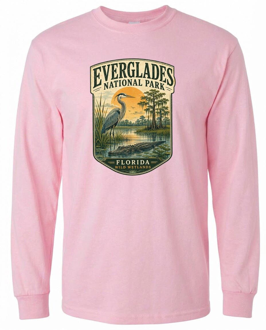 A pink long-sleeved t-shirt with a graphic design depicting a bird, likely a heron, standing in a marshy area with trees and a sunset in the background.