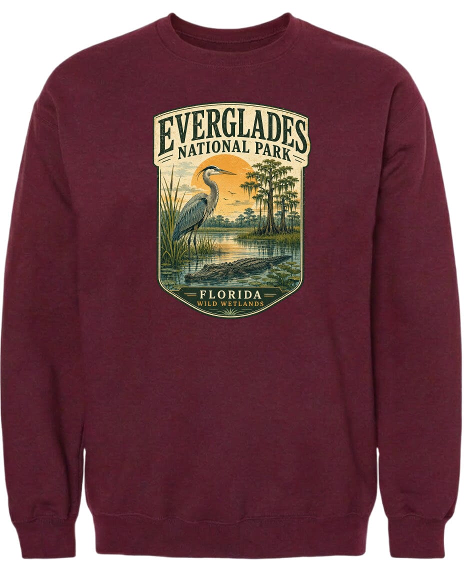 A maroon sweatshirt with a graphic design depicting a bird, likely a heron, standing in a marshy area with trees and a sunset in the background.