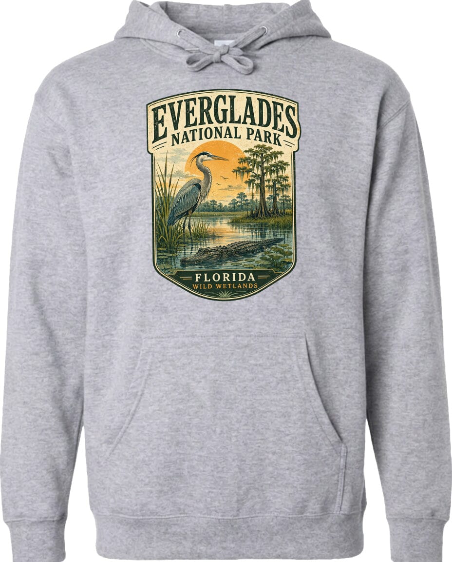A gray hoodie with a graphic design depicting a bird standing in a marshy area with trees and a sunset in the background.