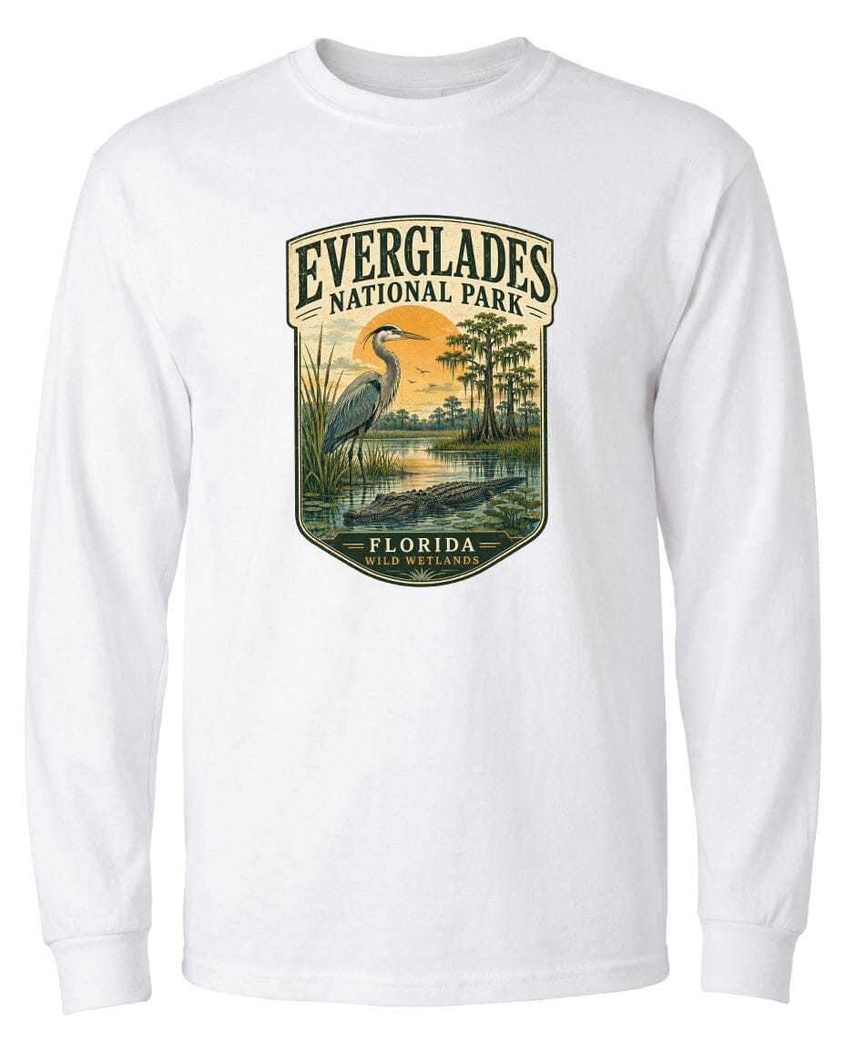 A white long-sleeved t-shirt with a graphic design depicting a bird, likely a heron, standing in a marshy area with trees and a sunset in the background.