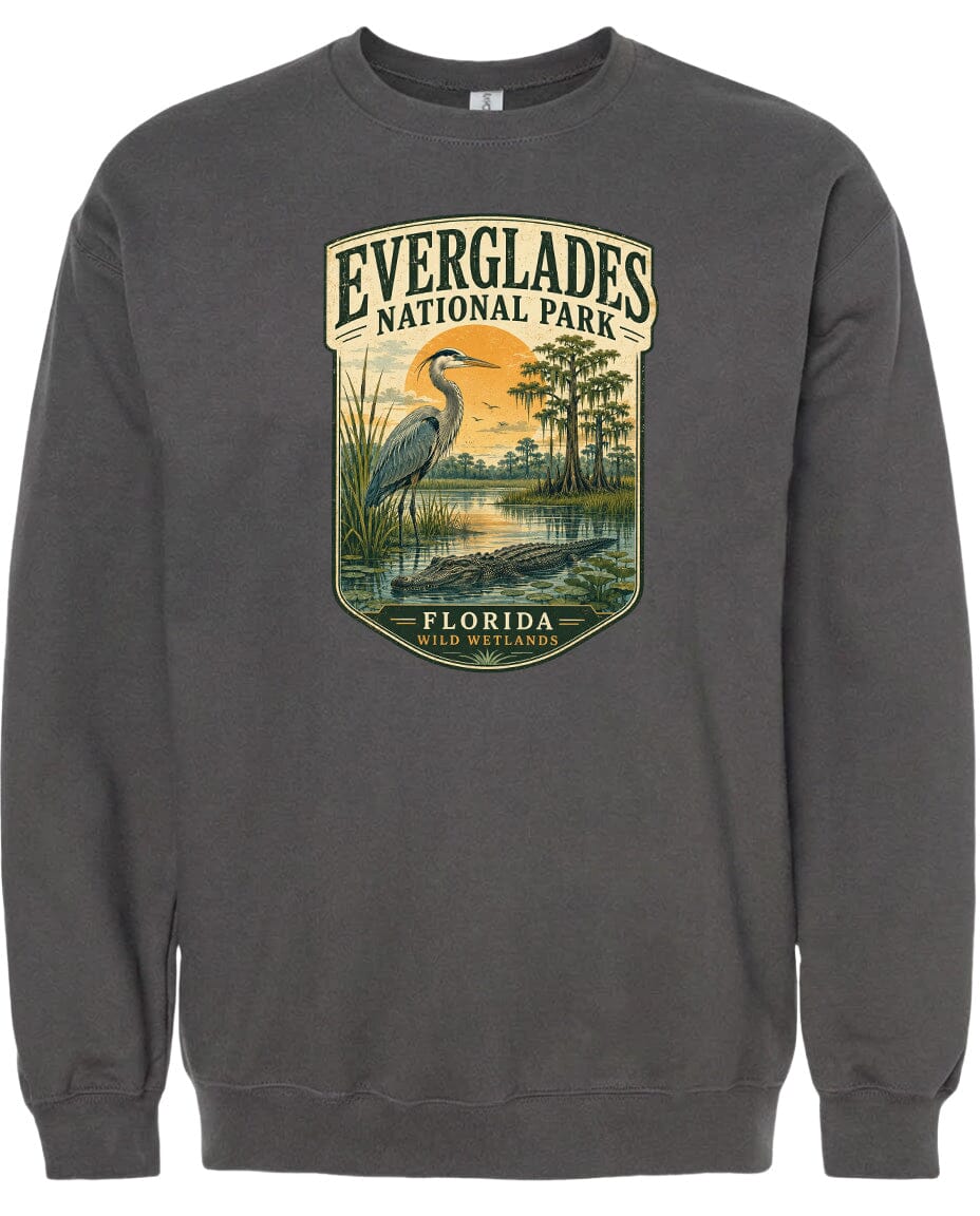 A gray sweatshirt with a graphic design depicting a bird, likely a heron, standing in a marshy area with trees and a sunset in the background.