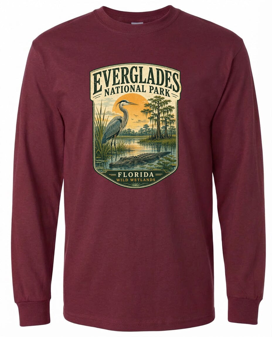 A long-sleeved burgundy t-shirt with a graphic design depicting a bird, likely a heron, standing in a marshy area with trees and a body of water.