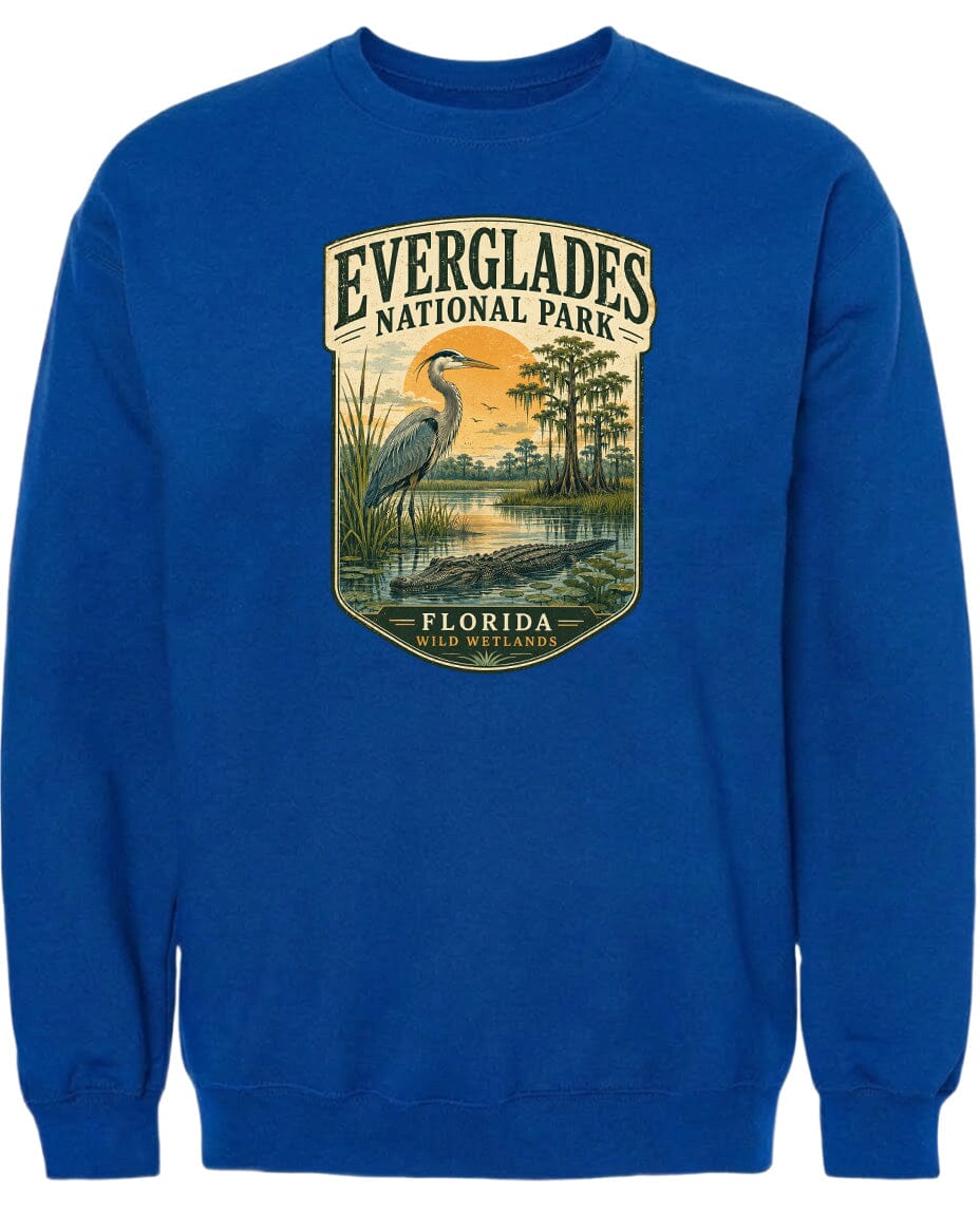 A blue sweatshirt with a graphic design depicting a bird, likely a heron, standing in a marshy area with trees and a sunset in the background.